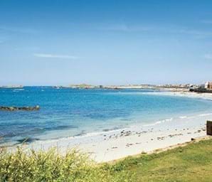view of cobo bay in guernsey with white sand and green grass