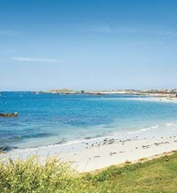 view of cobo bay in guernsey with white sand and green grass