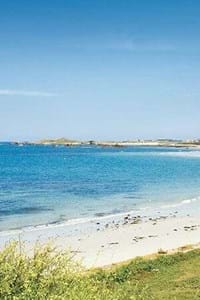 guernsey beach with grassy hills, white sand and blue sky