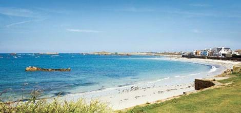 guernsey beach with grassy hills, white sand and blue sky